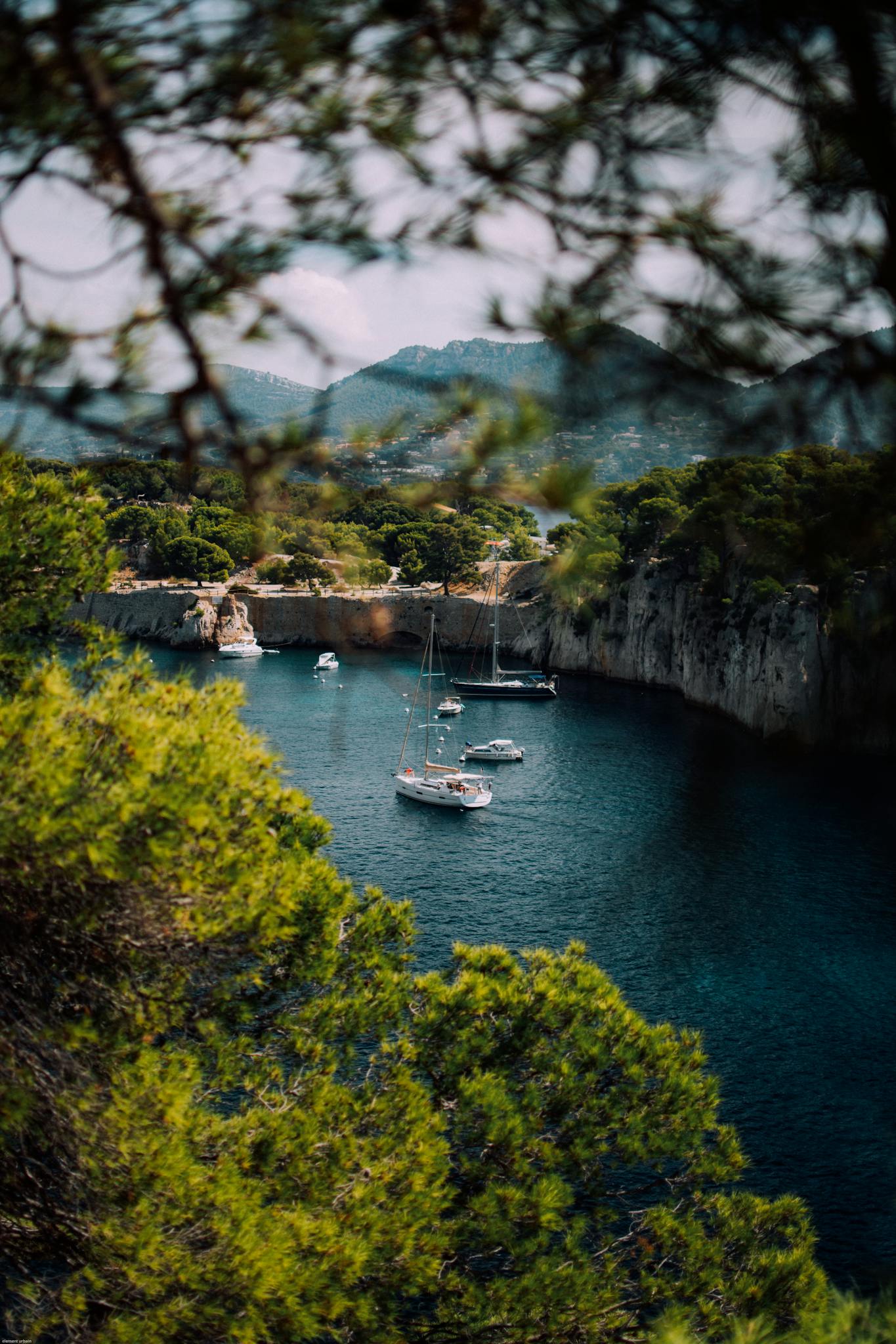 A picturesque Mediterranean cove with sailboats surrounded by lush greenery.