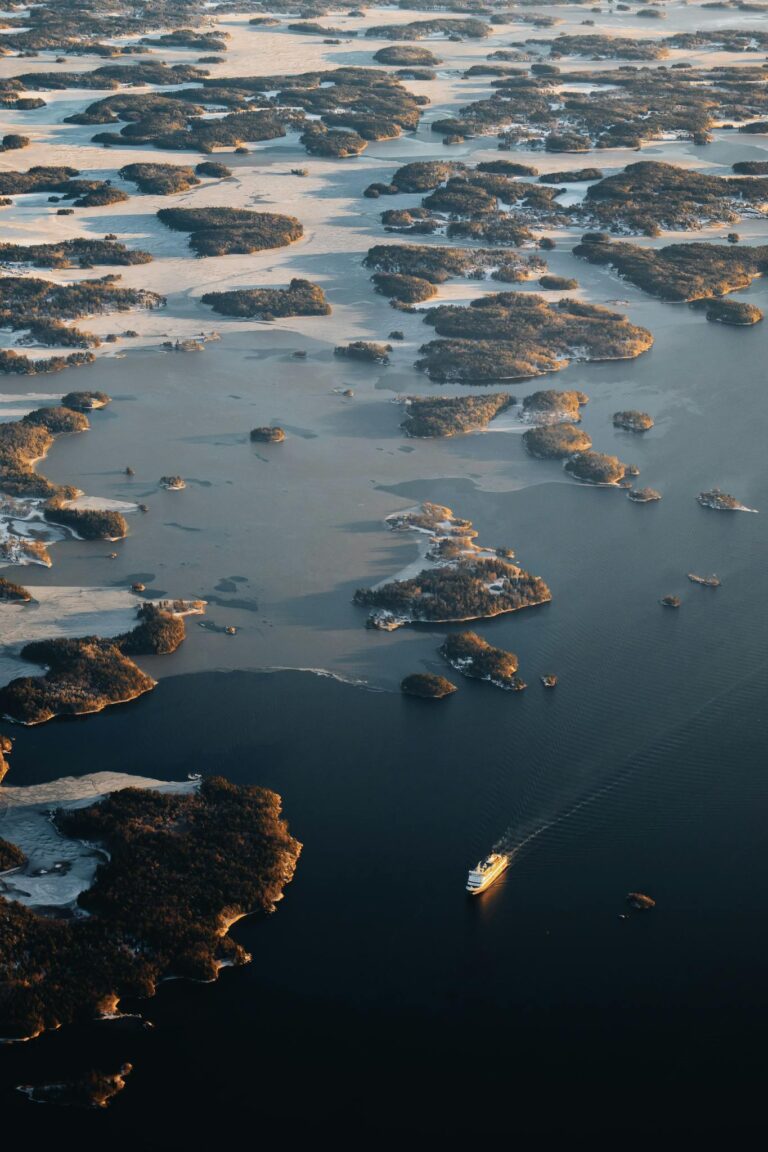 Aerial shot of a ship navigating through Sweden's archipelago at sunset.