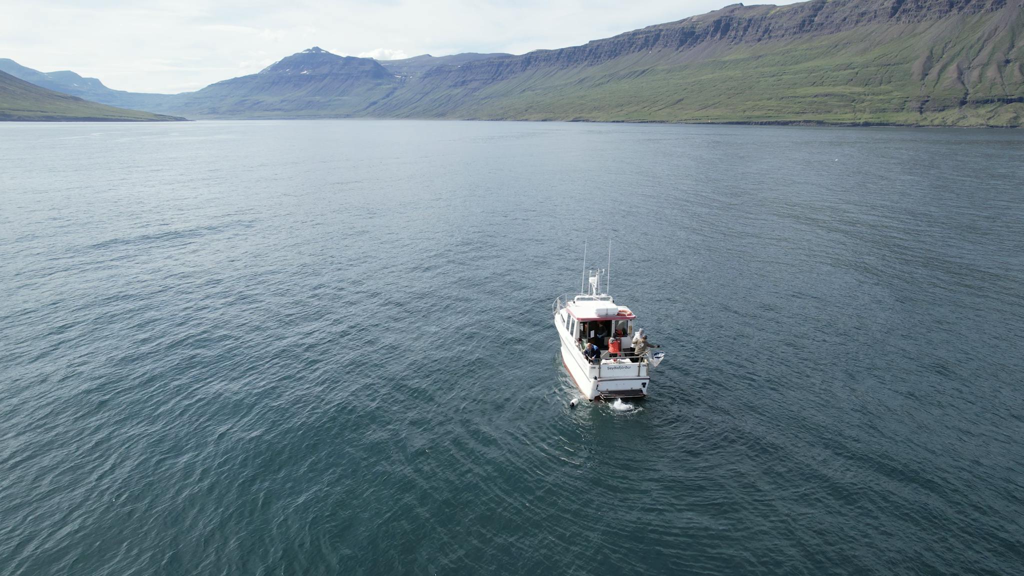 Dramatic aerial view of a motorboat on a serene lake with mountainous backdrop in Seydisfjordur, Iceland.