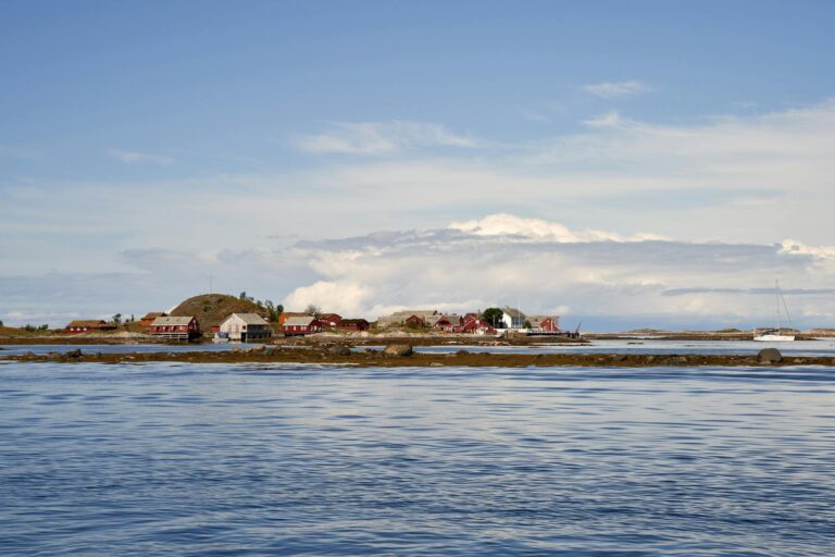 Picturesque view of a waterfront village with red houses by a serene sea under a clear sky.
