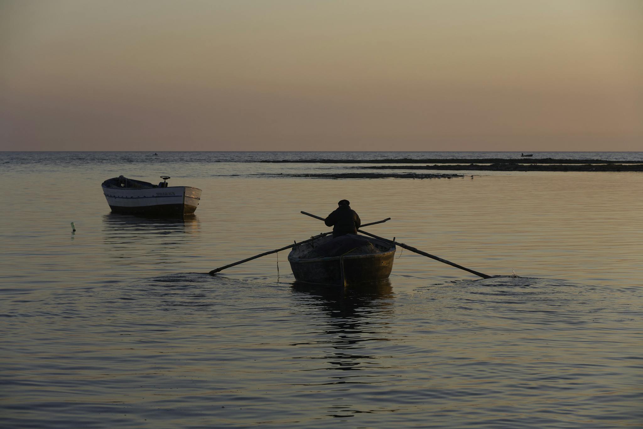 Serene scene of a lone rower navigating tranquil waters at sunset in Porto Cesareo, Italy.